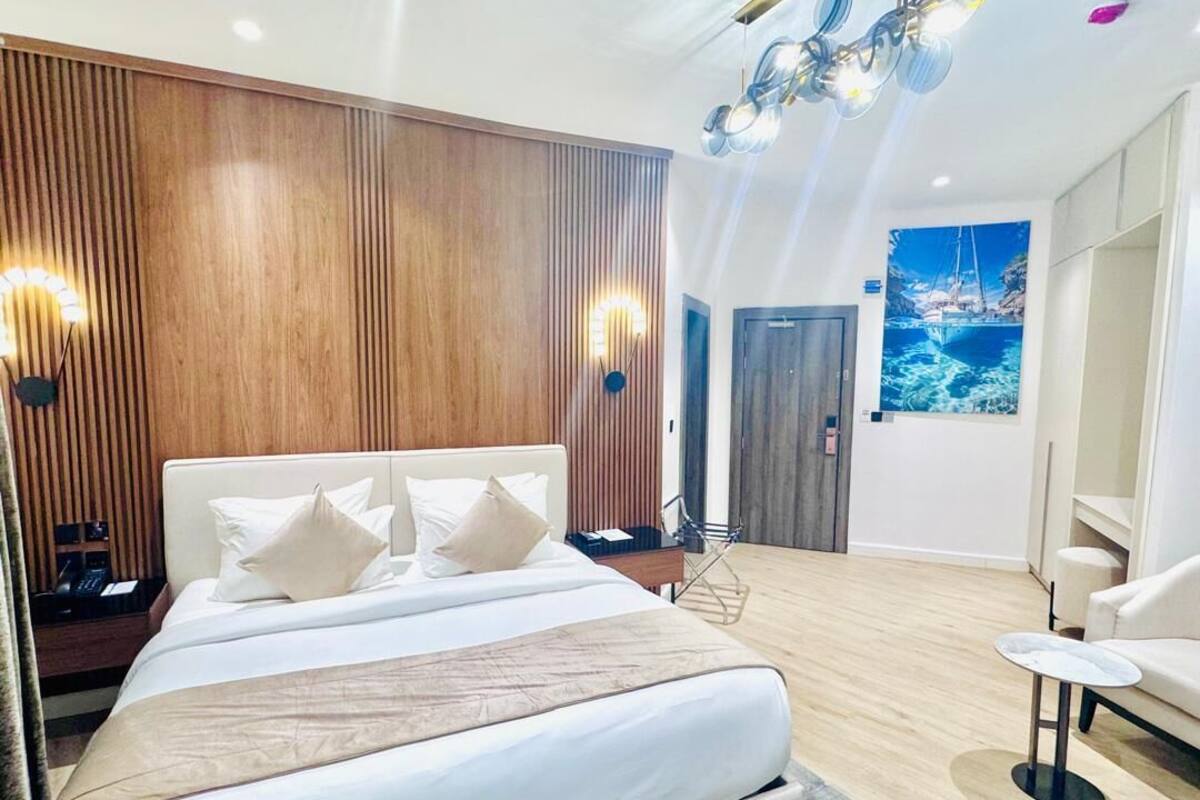 A modern hotel room with a large bed, wooden paneling on the walls, a painting of a boat on the wall, and a small round table.