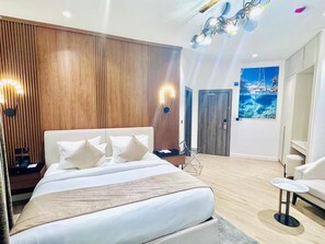 Ein modernes Hotelzimmer mit einem großen Bett, Holzvertäfelung an den Wänden, einem Gemälde eines Bootes und einem kleinen runden Tisch.
