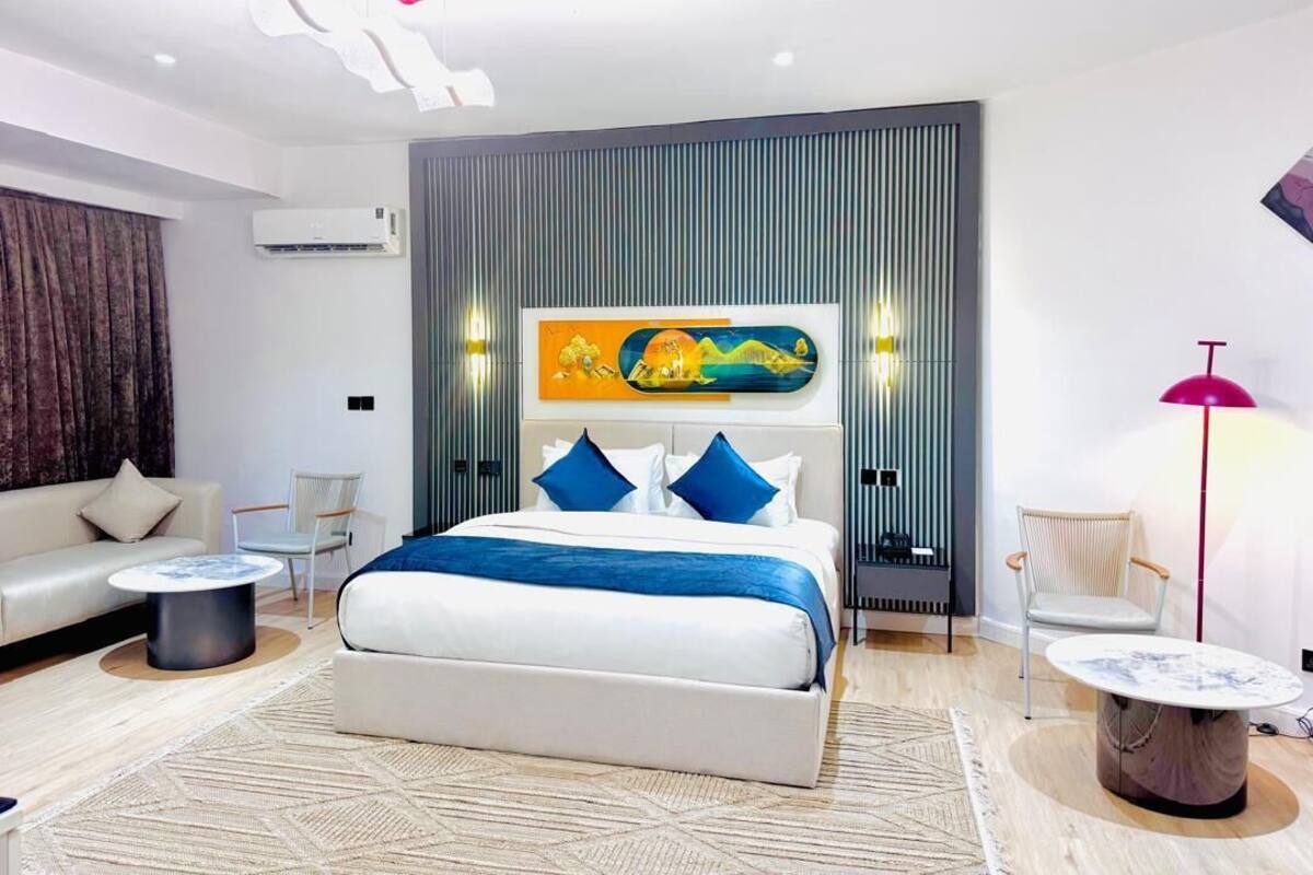 A modern hotel room with a large bed, a sofa, a coffee table, and a floor lamp.