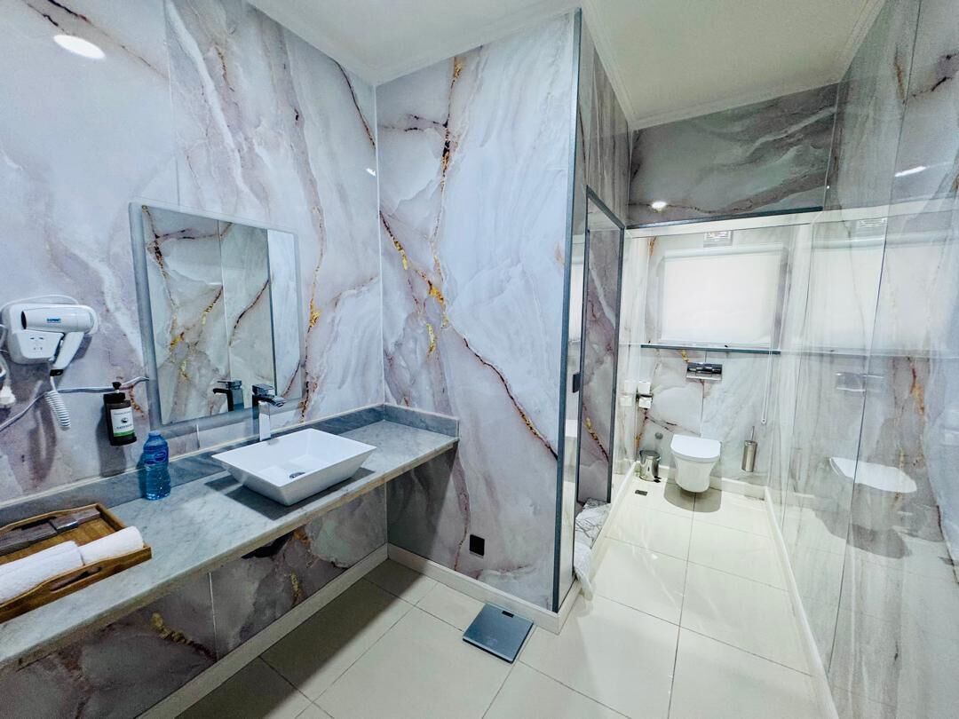 A modern bathroom with a marble vanity, a glass shower enclosure, and a separate toilet area.