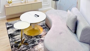 A modern living room with a large flat-screen TV, a white sofa, a round coffee table, and a floor lamp. - ATLANTIS HOTELS (Lagos)