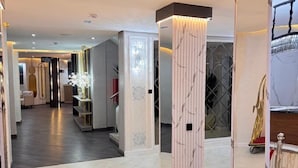A modern hotel lobby with a clean, minimalist design, featuring a central column with a lighted base, a clothing display, and a spacious layout. - ATLANTIS HOTELS (Lagos)