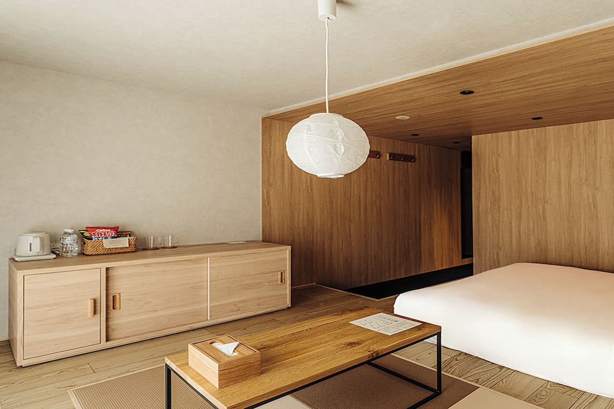 Una habitación de hotel moderna con una cama y una mesita de noche de madera, un escritorio y una lámpara colgante.