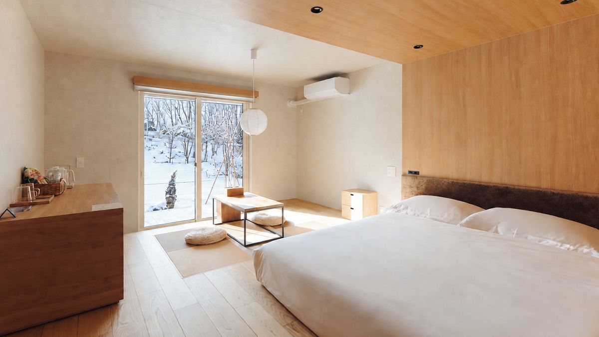 A modern bedroom with a large bed, a wooden dresser, a desk, and a view of a snowy landscape through the window.