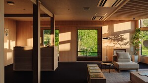 A modern interior with a reception desk, a seating area with a sofa and armchairs, a coffee table, and a large window providing a view of greenery. - LANSHAN HOTEL  (Naganuma)