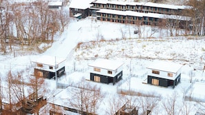 Un ensemble immobilier moderne composé de plusieurs bâtiments, dont un bâtiment principal doté d’un toit plat et de plusieurs bâtiments plus petits, également à toit plat, le tout étant entouré d’un paysage enneigé.