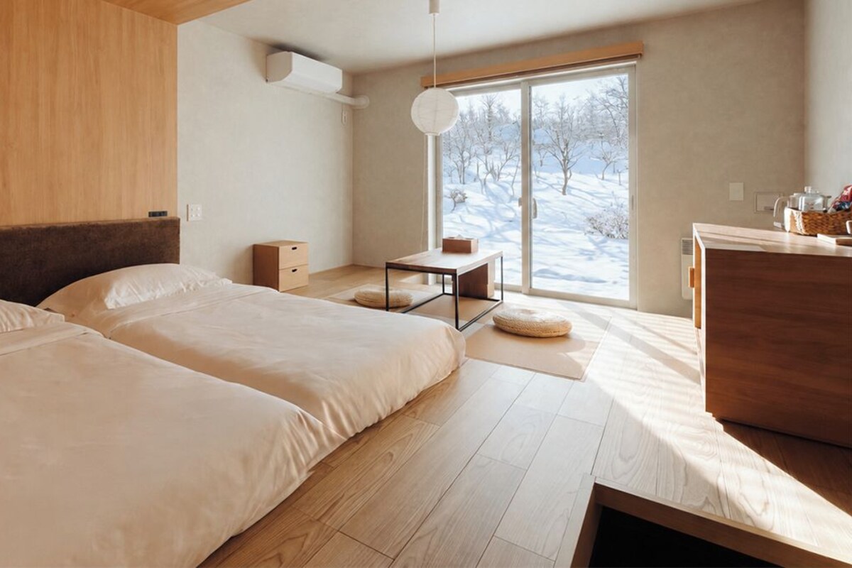 A modern bedroom with two beds, a wooden desk, and a large window with a view of a snowy landscape.