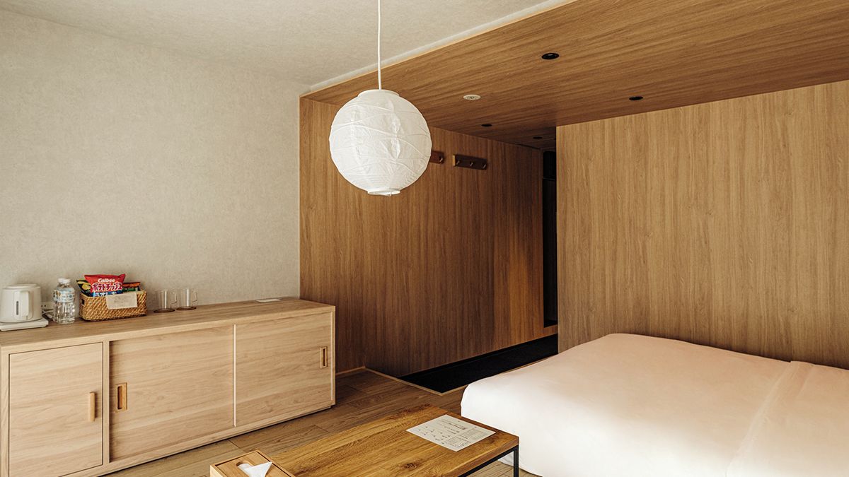 A modern hotel room with a wooden wardrobe, a bedside table, and a hanging light fixture.