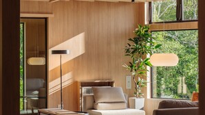 A modern living room with a sofa, a coffee table, and a potted plant. There is a large window providing natural light and a view of greenery outside. - LANSHAN HOTEL  (Naganuma)