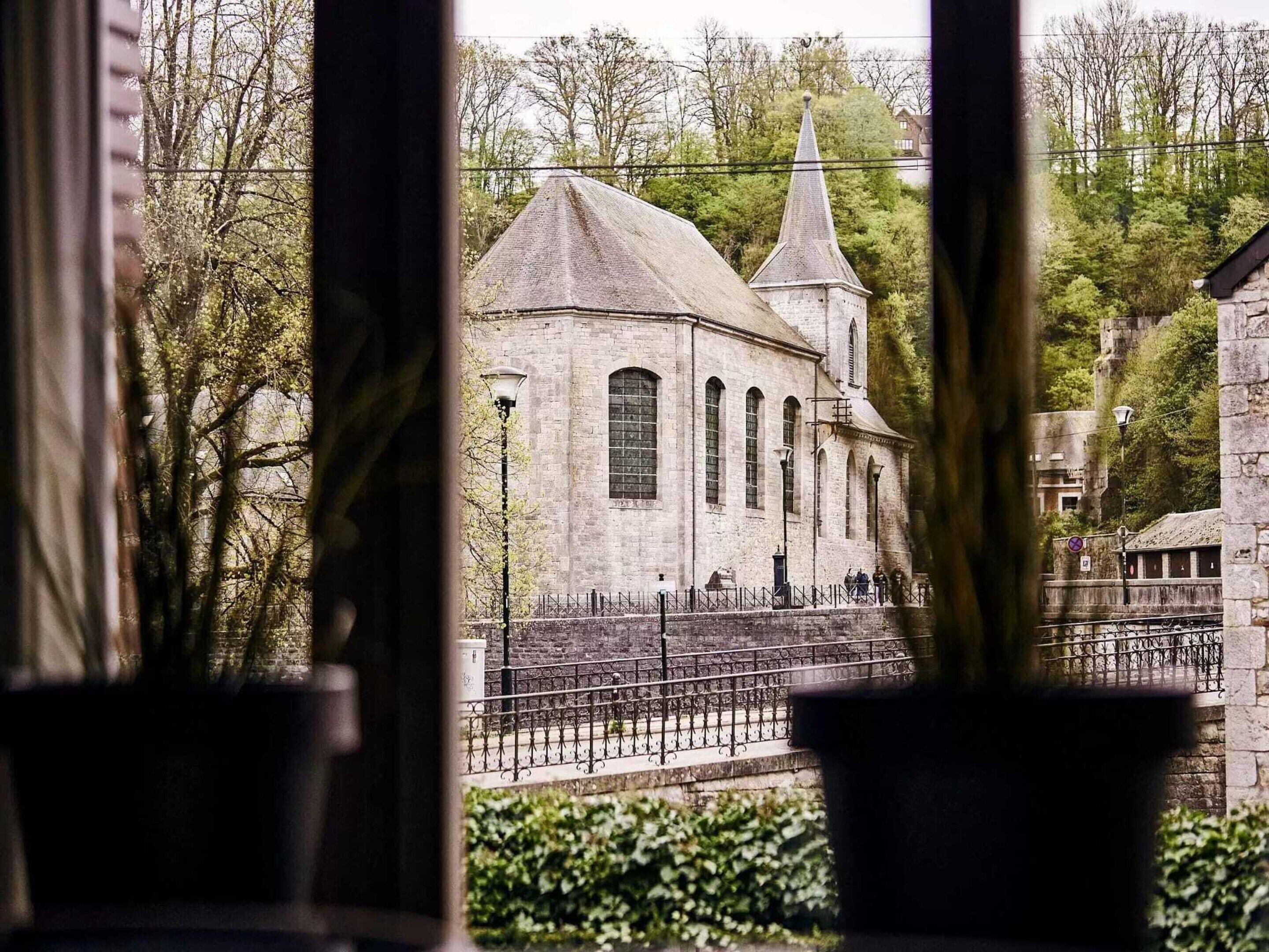 A historic building with a prominent tower and arched windows, viewed through a window with potted plants.