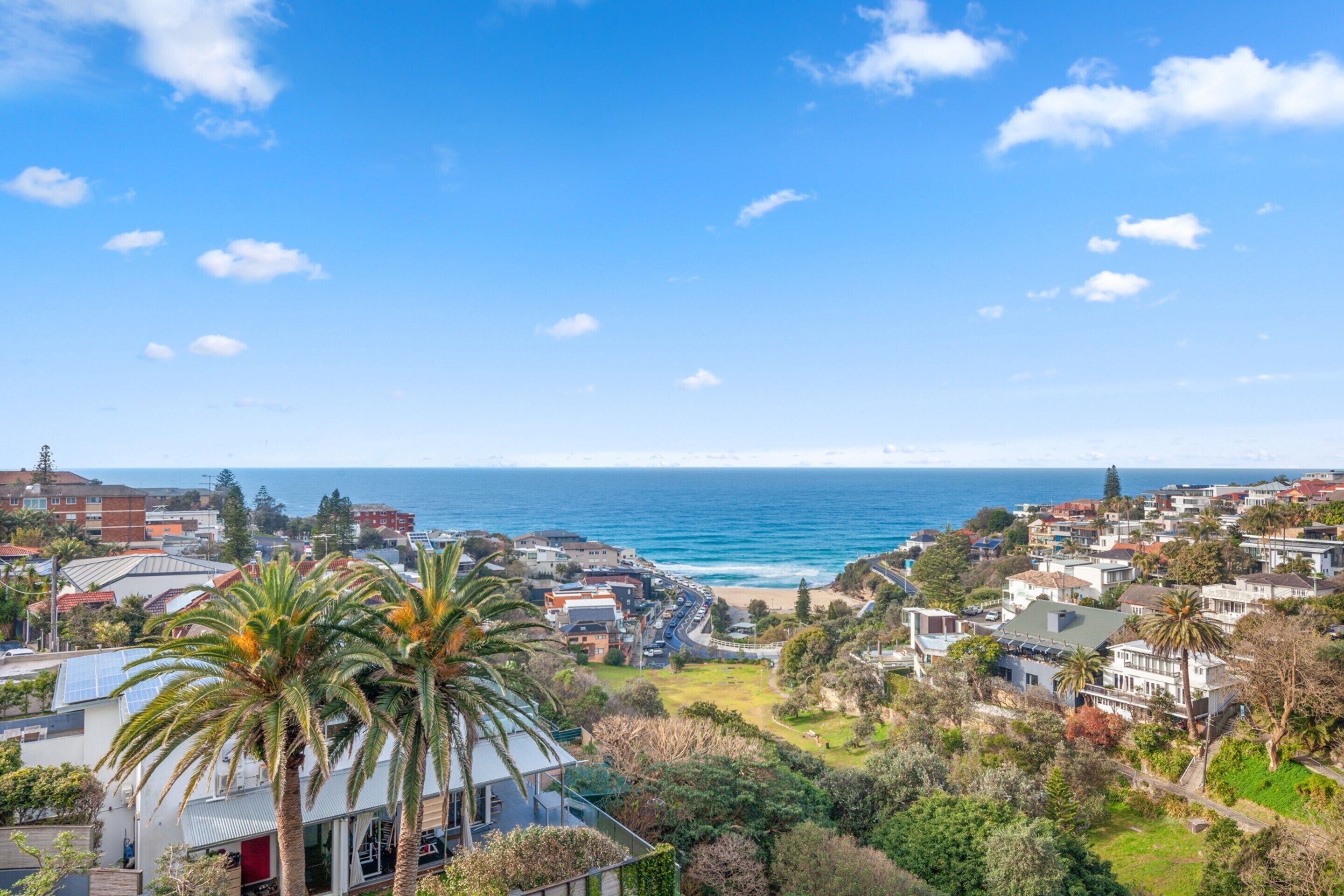 A coastal residential area with houses, a beach, and a clear blue sky.
