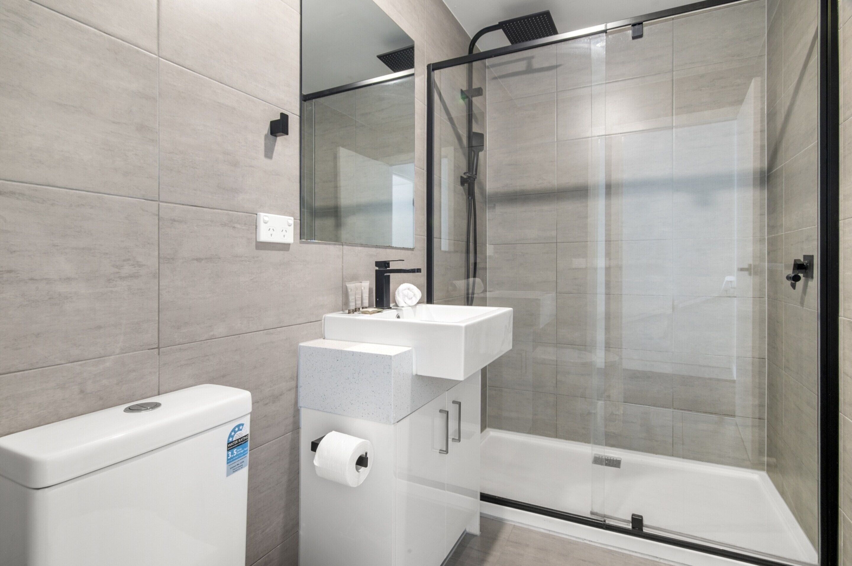 A modern bathroom with a glass-enclosed shower, a white sink, and a toilet.