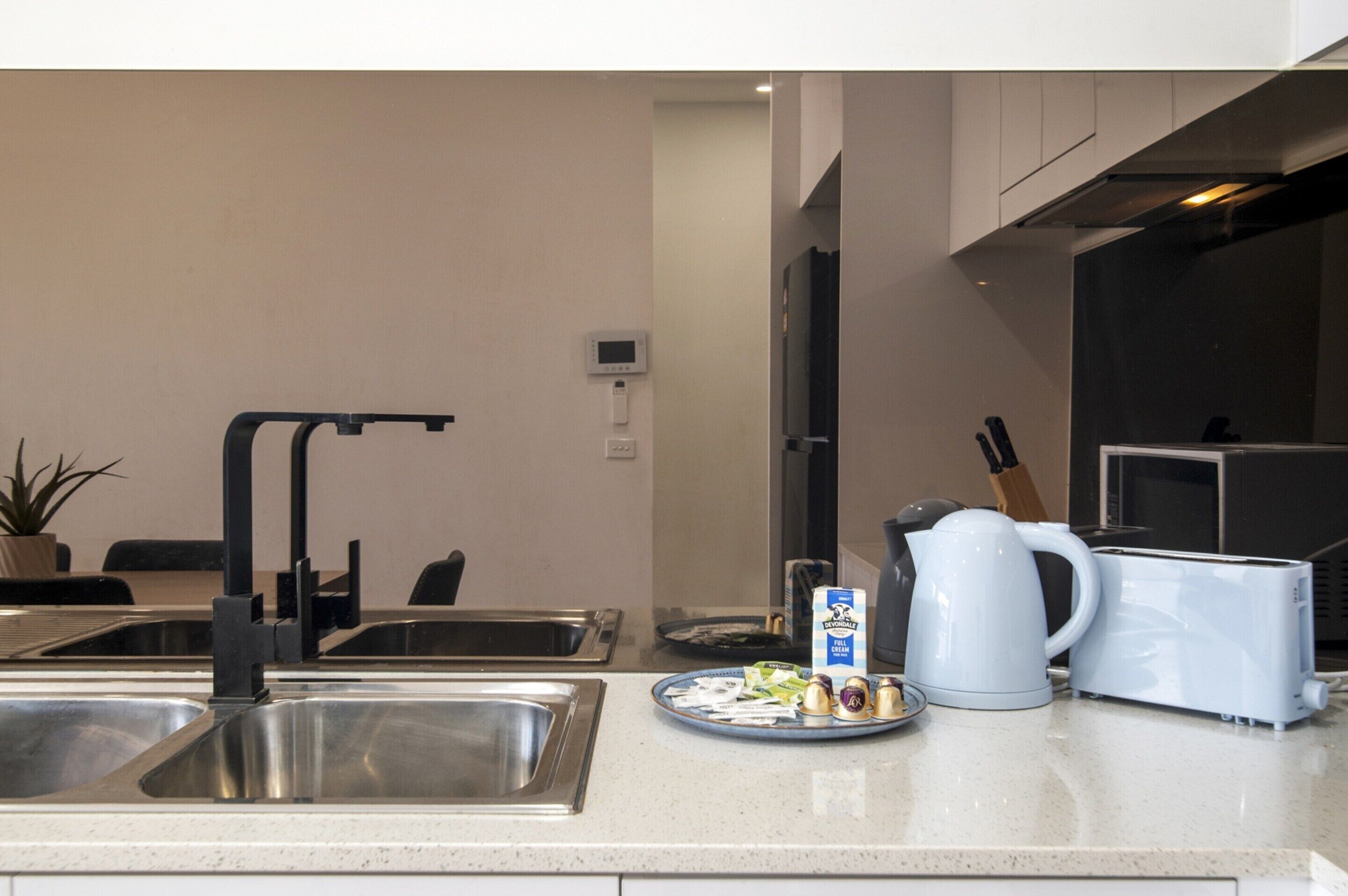 A modern kitchen with stainless steel sinks, a coffee maker, a toaster, and a microwave.