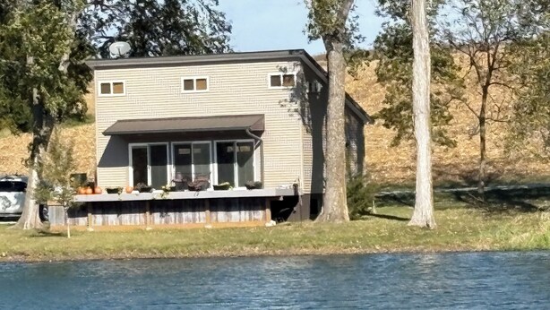 A house by a lake with a covered porch and a satellite dish.