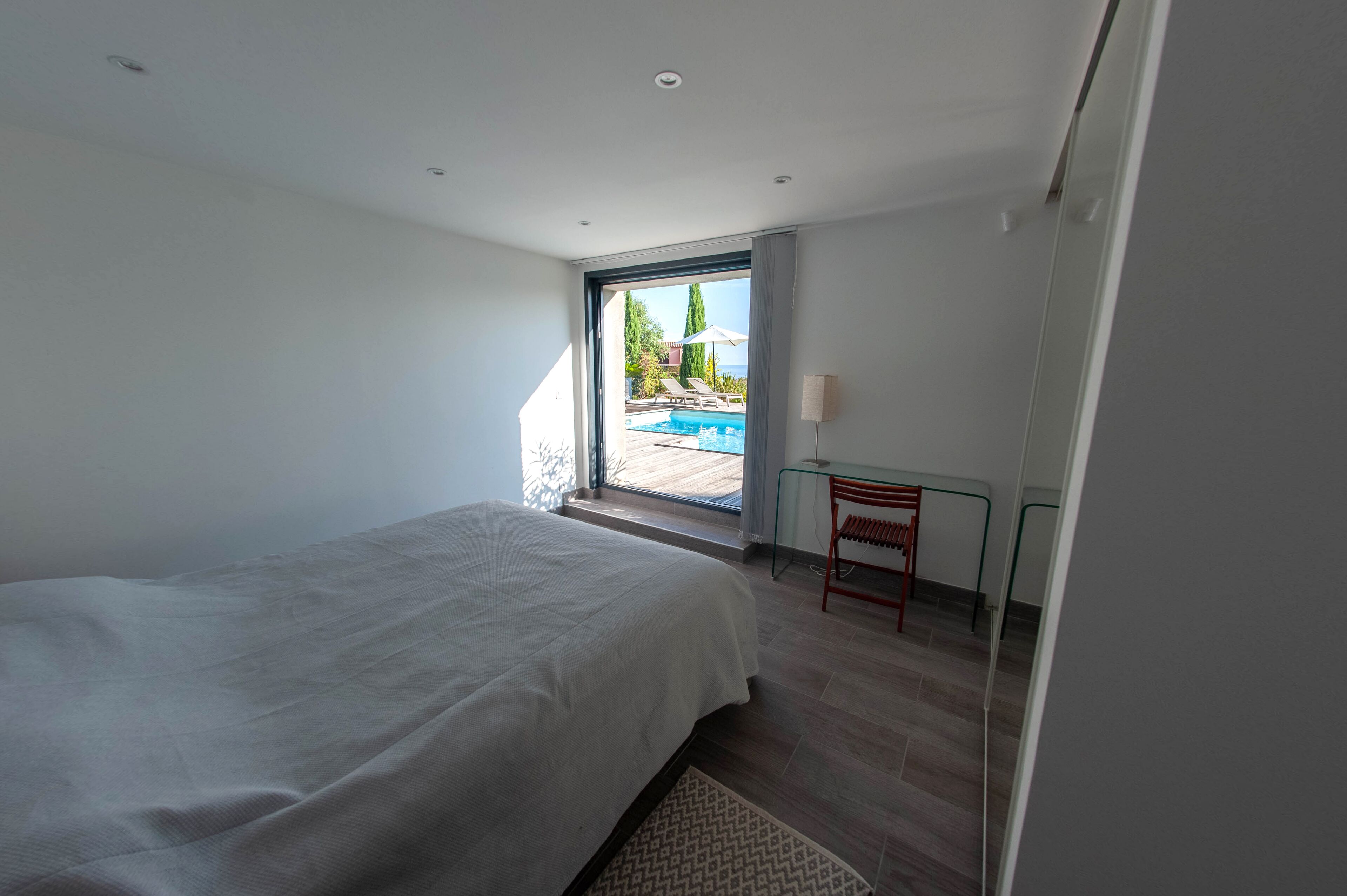 A bedroom with a large bed, a glass door leading to a balcony with a pool view.