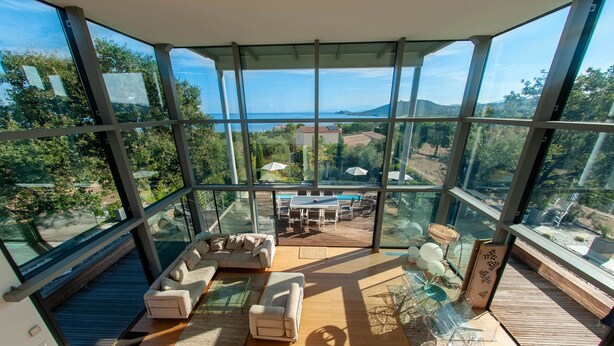 A modern living room with large glass windows, a sofa set, a dining table, and a view of the sea and hills. - Design villa, air-conditioned, heated swimming pool Marine de davia, corbara l'ile Rousse (Corbara)