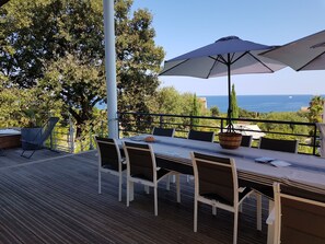 An outdoor dining area with a table, chairs, and umbrellas, overlooking a scenic view of the sea. - Design villa, air-conditioned, heated swimming pool Marine de davia, corbara l'ile Rousse (Corbara)