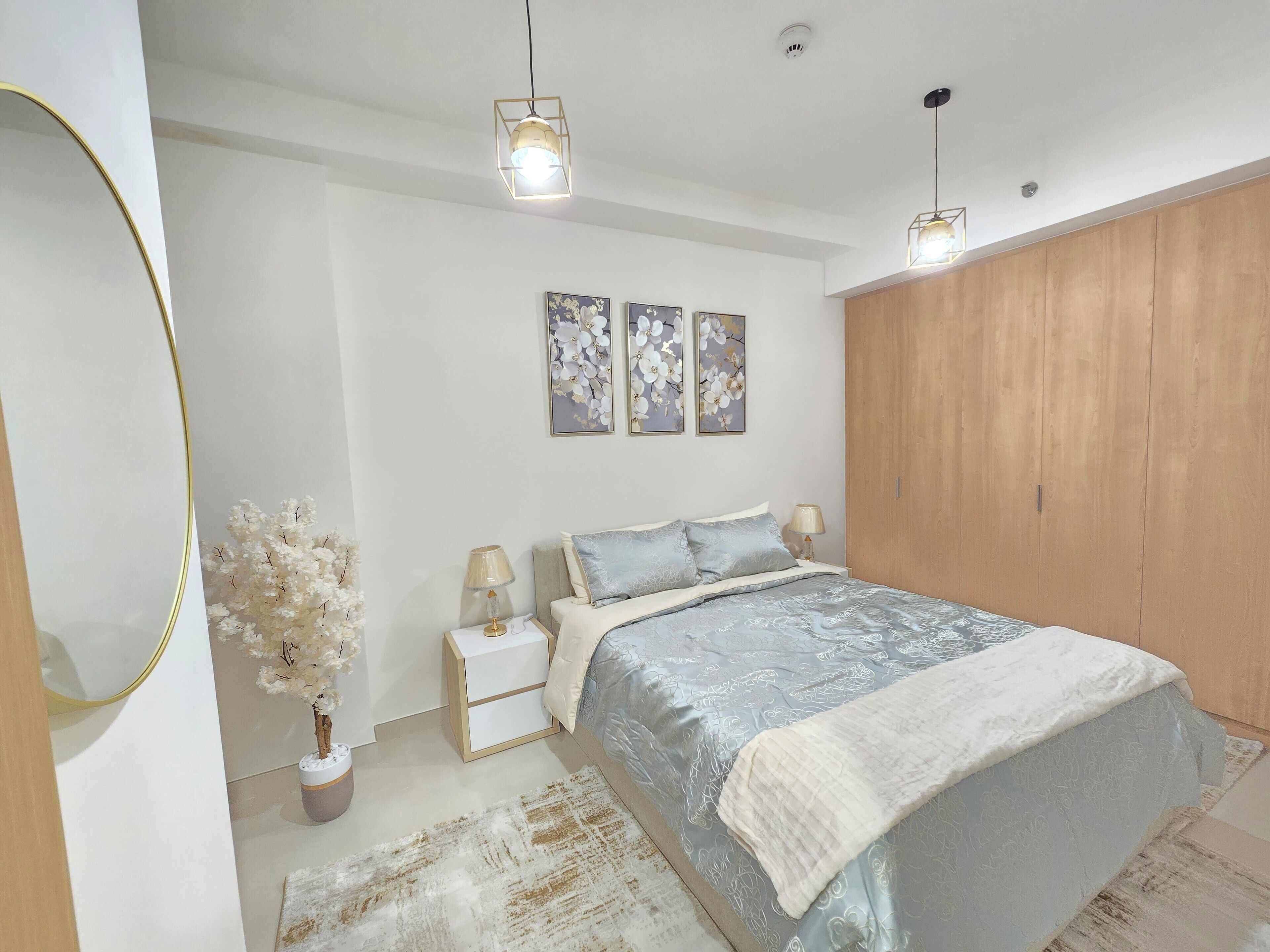Un dormitorio con cama, mesitas de noche, tocador, espejo, armario y decoración en la pared.