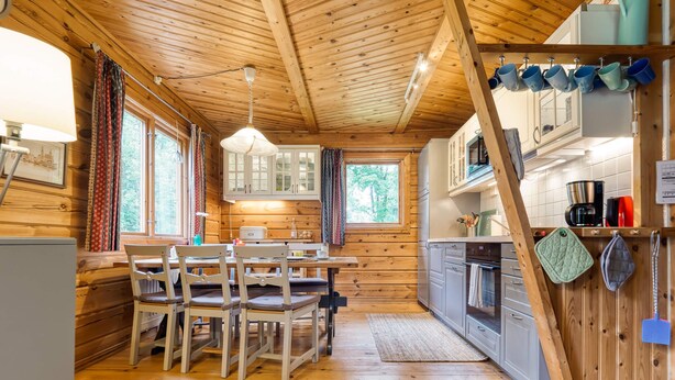 Interno di una baita in legno con zona pranzo, cucina e ampie finestre.