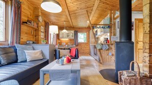 Un accogliente interno di una baita con soffitto in legno, un divano, un tavolo da pranzo e una zona cucina.
