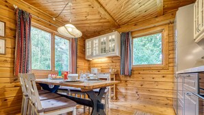 Interno di una baita in legno con tavolo da pranzo, sedie, angolo cottura e ampie finestre.