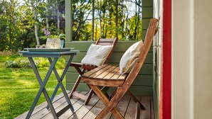 Un terrazzo in legno con un tavolo e due sedie, una piccola pianta in vaso e vista su un paesaggio verde con alberi.