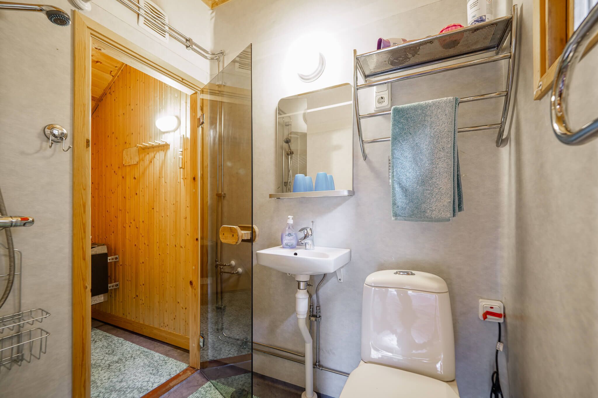 Een badkamer met een houten deur, een glazen douchecabine, een wit wastafelmeubel en een toilet.