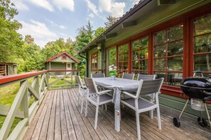 Eine Holzterrasse mit Tisch und Stühlen, einem Grill und einem kleinen Schuppen im Hintergrund.