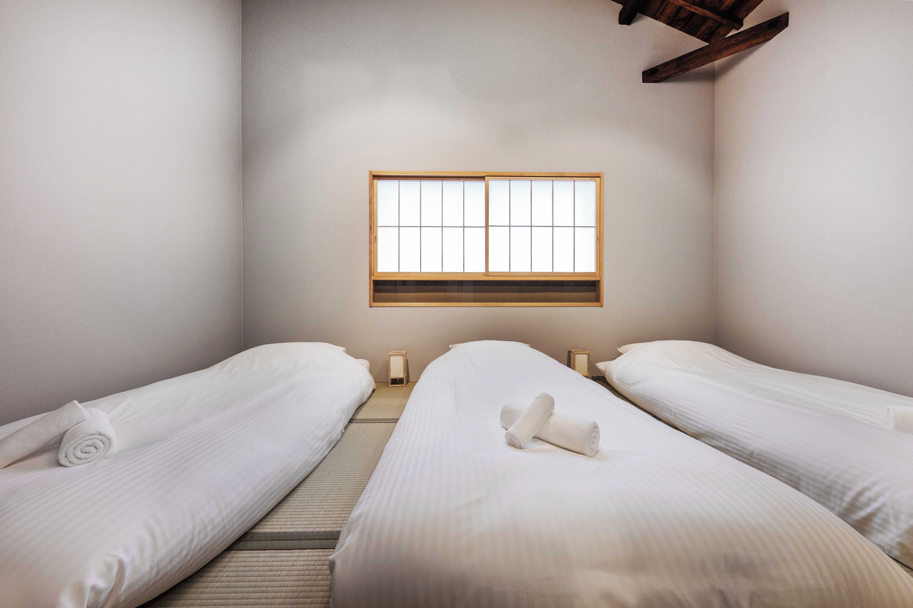 A hotel room with two beds, a large window, and a wooden ceiling beam.