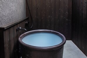 Una grande vasca da bagno rotonda e marrone piena d'acqua, addossata a un muro di legno dalla superficie irregolare.