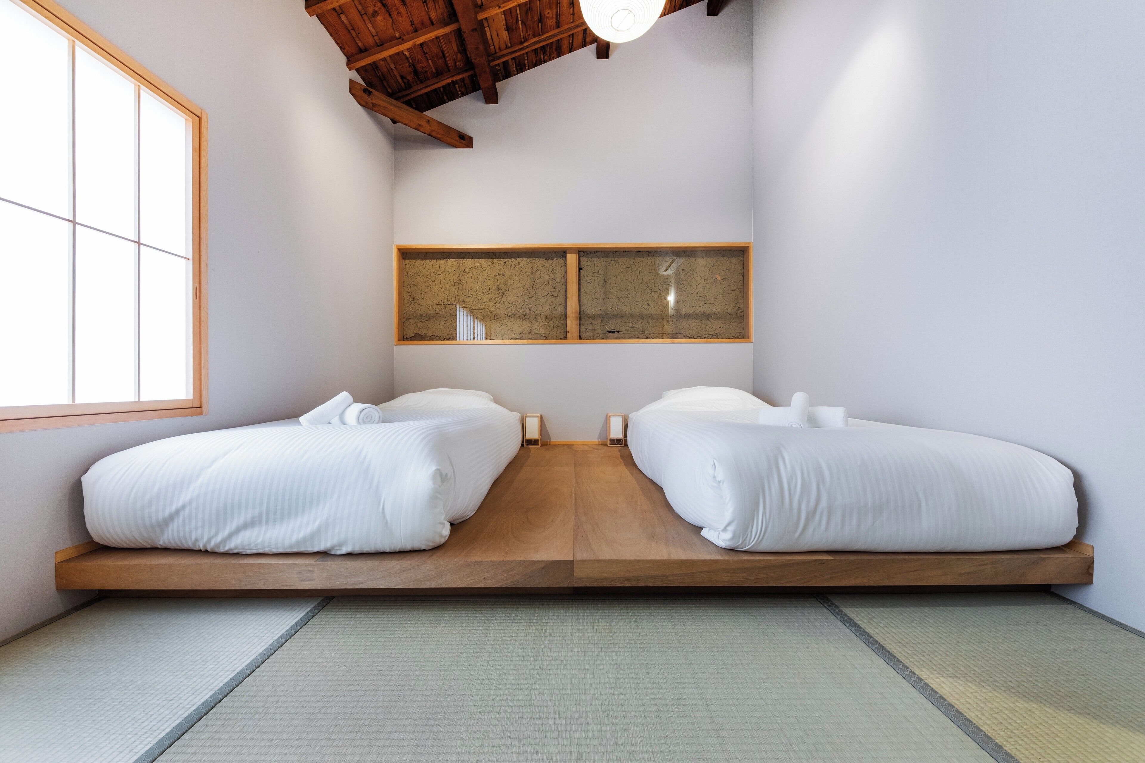 Una habitación minimalista con dos camas, un ventanal grande y techo de madera.