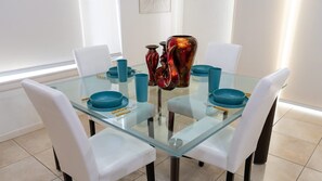 Un espace repas moderne avec une table en verre, des chaises blanches et de la vaisselle bleue.