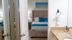Une chambre d’hôtel avec un lit, une salle de bain comprenant un lavabo et un porte-serviettes, et un tableau accroché au mur.