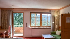 A room with a bed, a green sofa, a small table, and a window with a view of trees. - Hotel Gasthof Süßer Grund (Albstadt)
