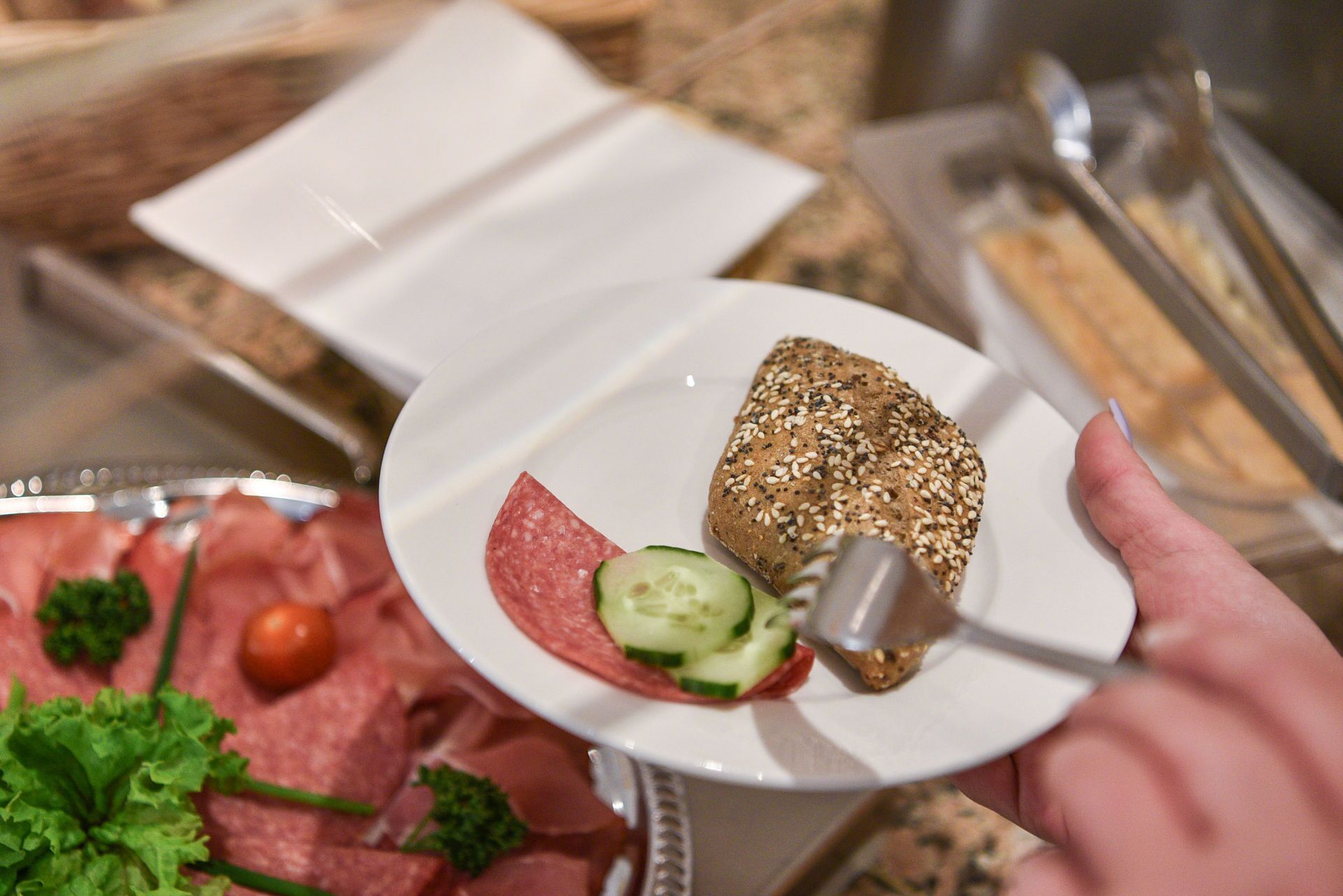 A plate with a slice of bread, a slice of salami, and a slice of cucumber.