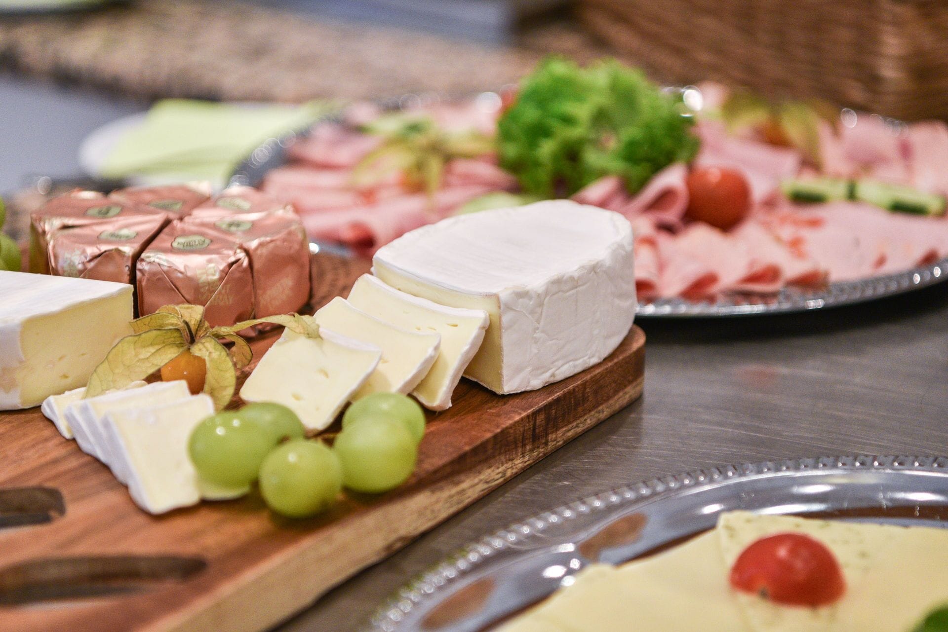 Una tabla de quesos con distintos quesos, uvas y una rodaja de tomate sobre una tabla de madera.
