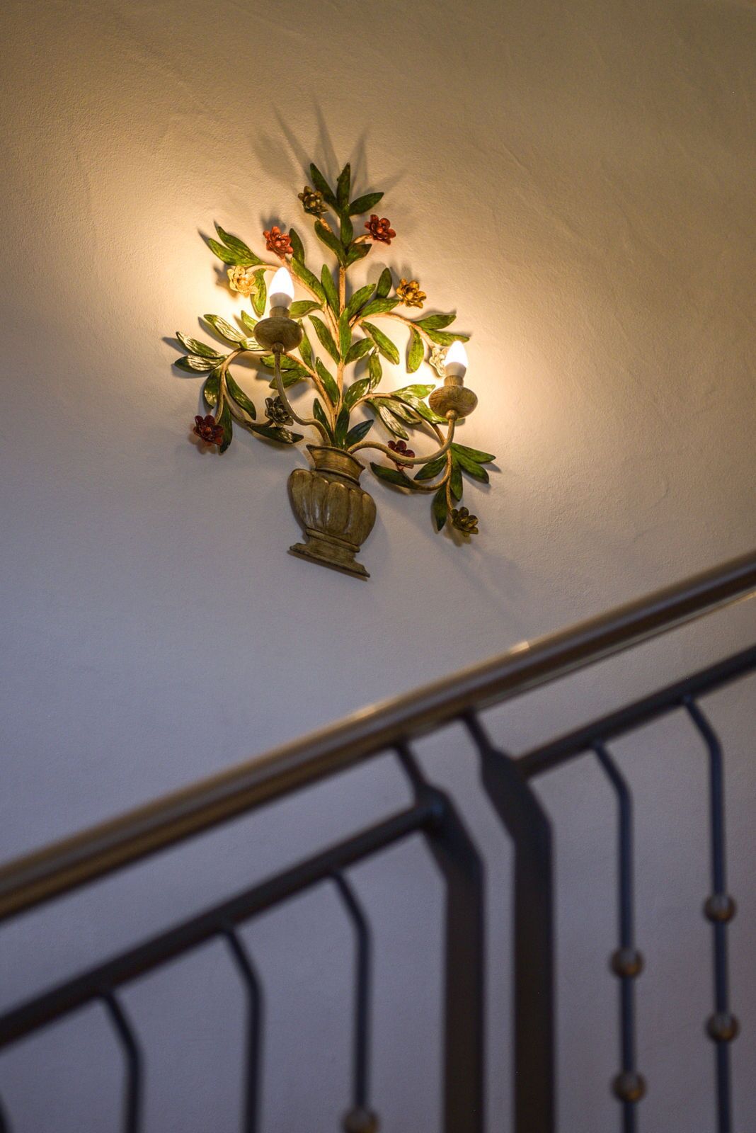 A wall-mounted light fixture with a floral design, including leaves and flowers, and a vase.