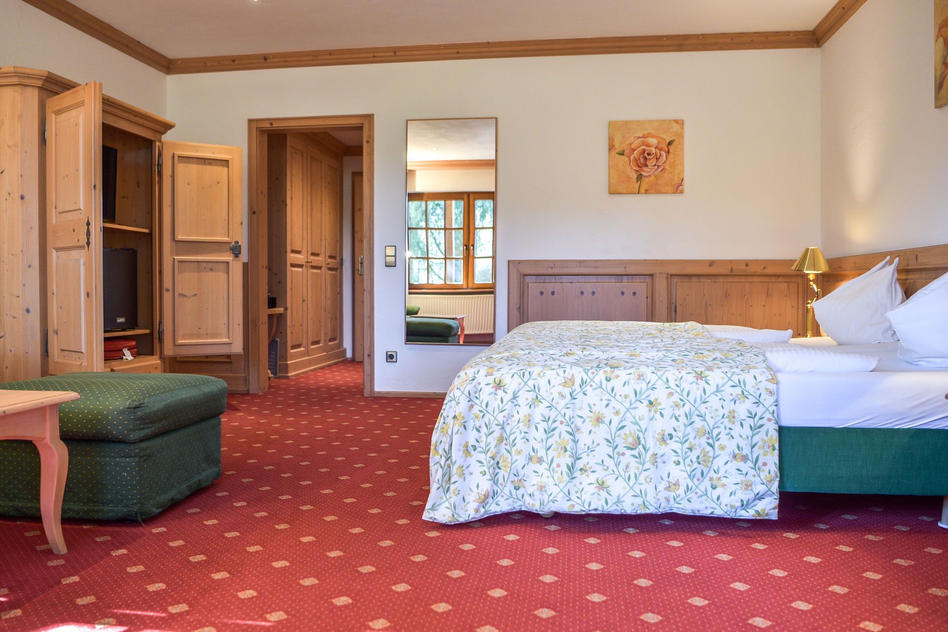 A bedroom with a bed, a green chair, wooden wardrobe, and a painting on the wall.