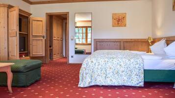 A bedroom with a bed, a green chair, wooden wardrobe, and a painting on the wall.