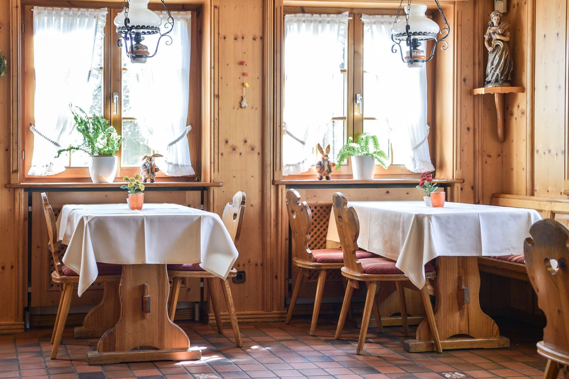 Un coin repas chaleureux, aménagé en bois, avec des tables et des chaises, des plantes en pot et une statue posée sur une étagère.