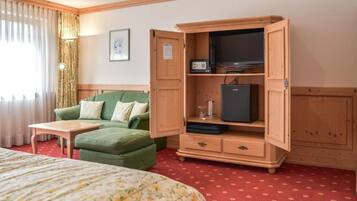 Habitación de hotel con cama, sofá verde, mueble de madera con televisor y refrigerador pequeño, y alfombra roja.