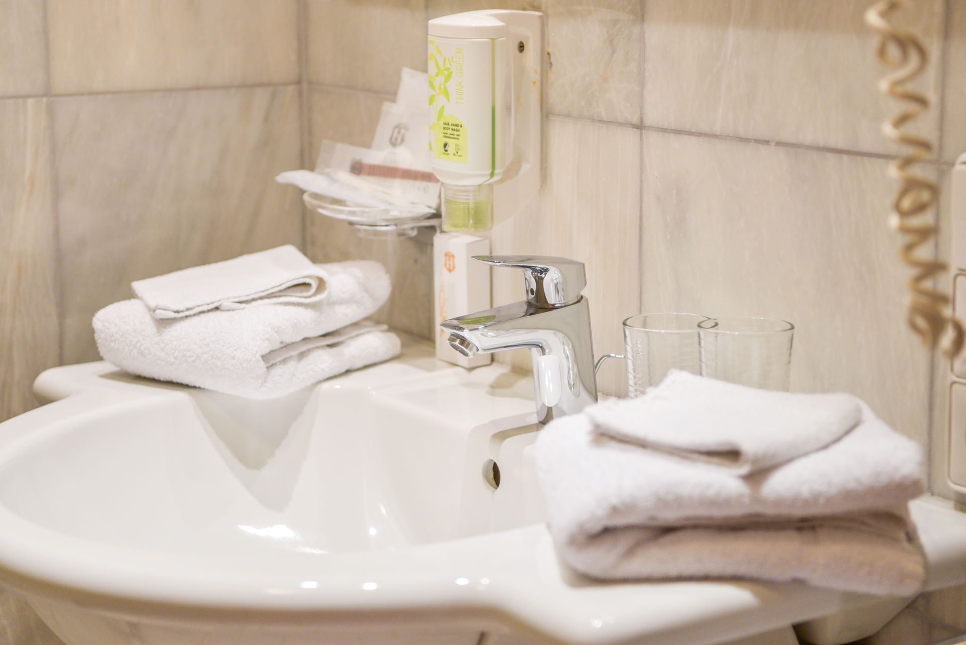 A bathroom sink with a hand soap dispenser, a glass, and folded towels.