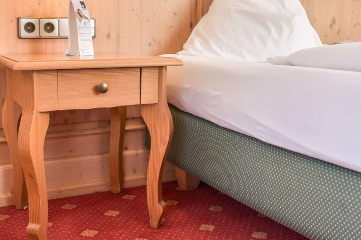 Una cama de madera con ropa de cama blanca, una mesita de noche con una lámpara y un cuadro en la pared.