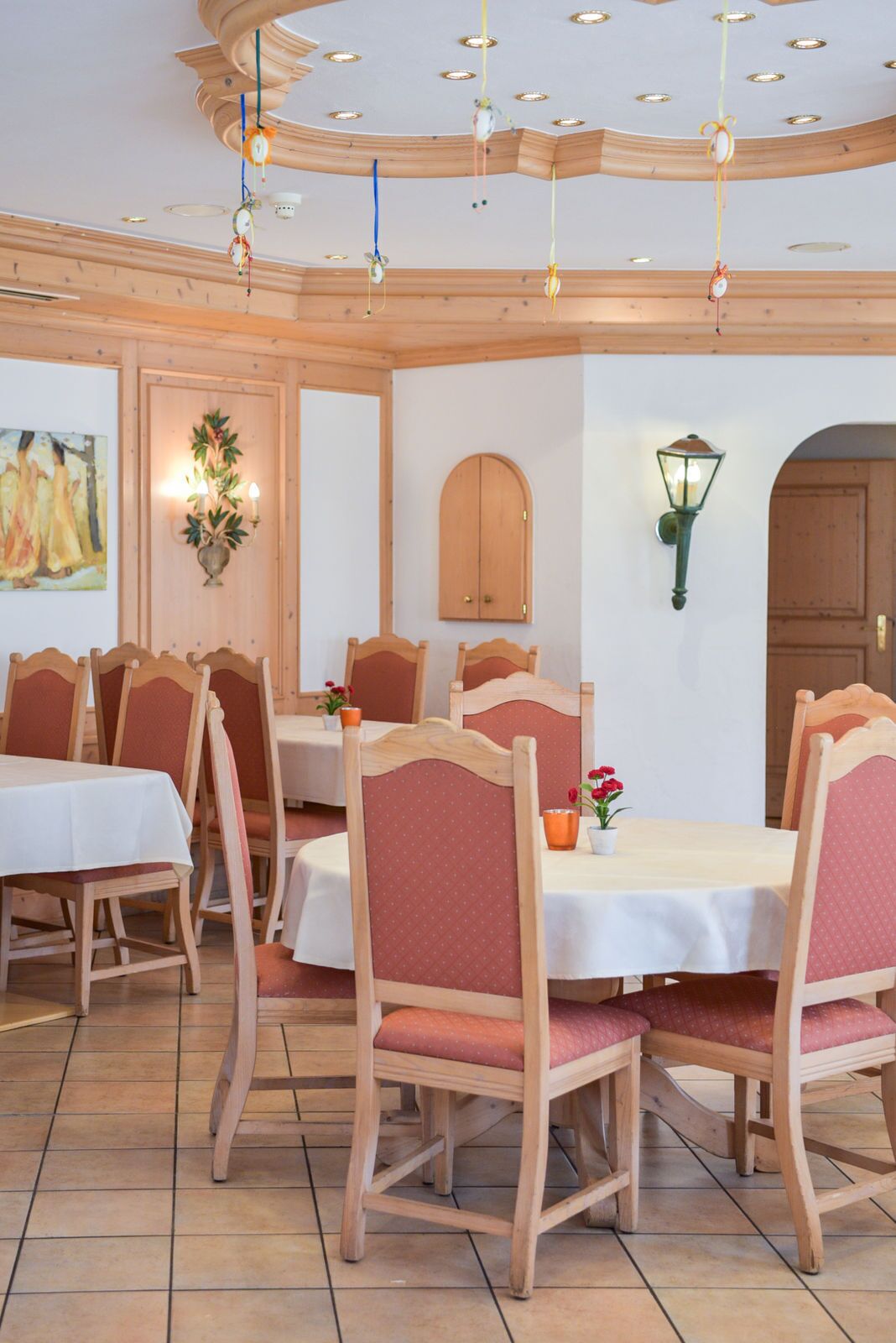 A dining area with wooden chairs and tables, a wooden ceiling with hanging lights, and a wall-mounted lamp.