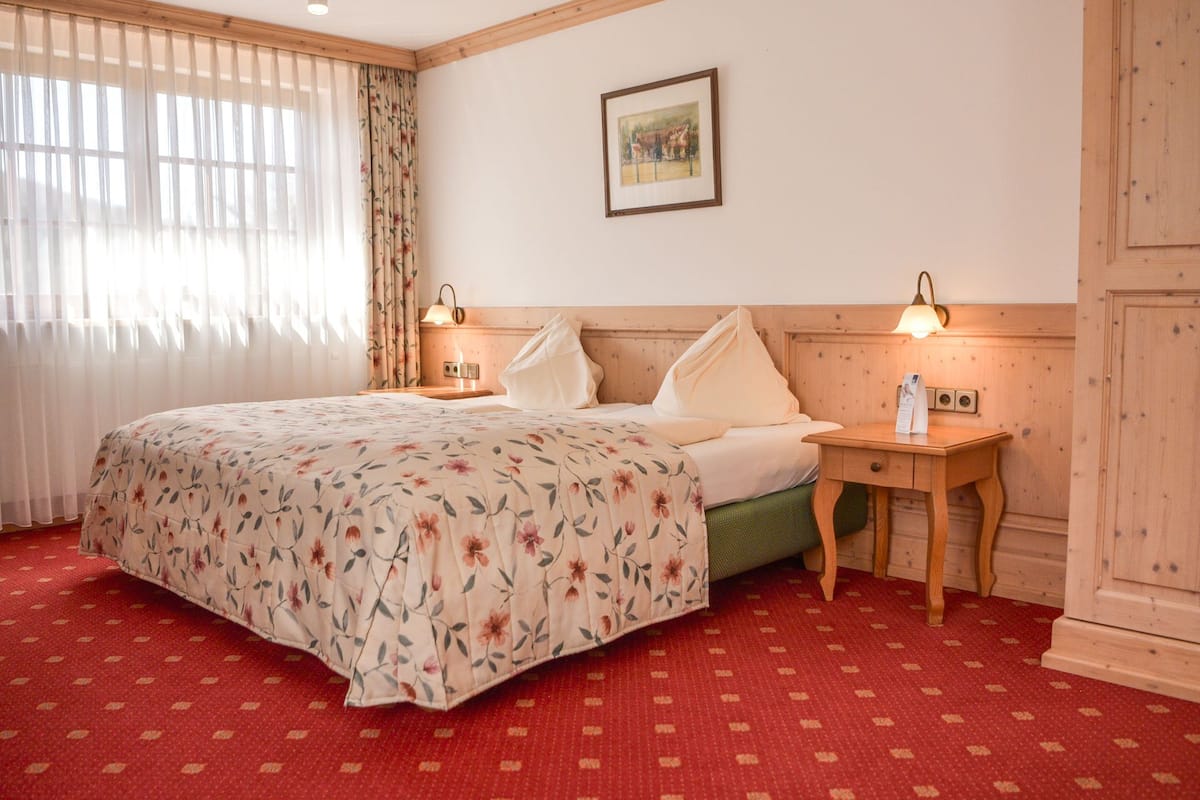 Habitación de hotel con cama, dos mesitas de noche, un armario de madera y un cuadro colgado en la pared.