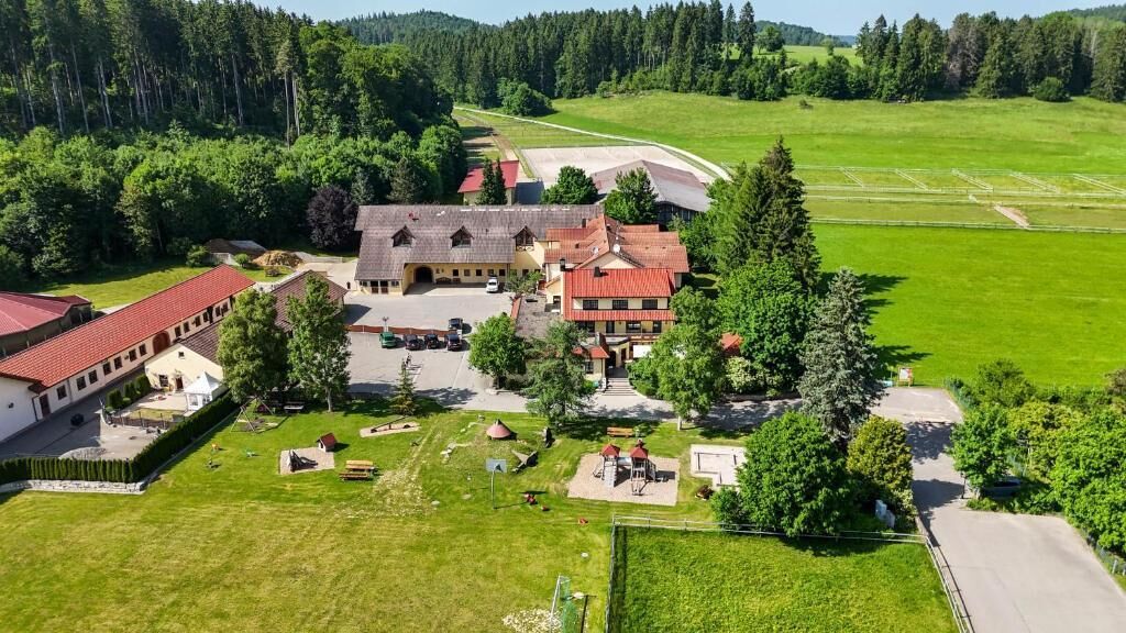 An aerial view of a rural property with multiple buildings, including a main house with a red roof, several smaller structures, and a large open field.
