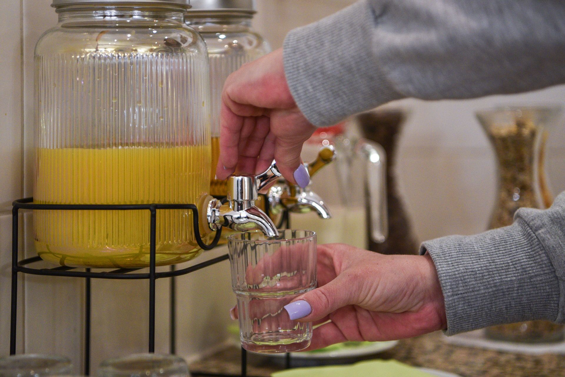 A person pouring a yellow liquid from a tap into a glass.