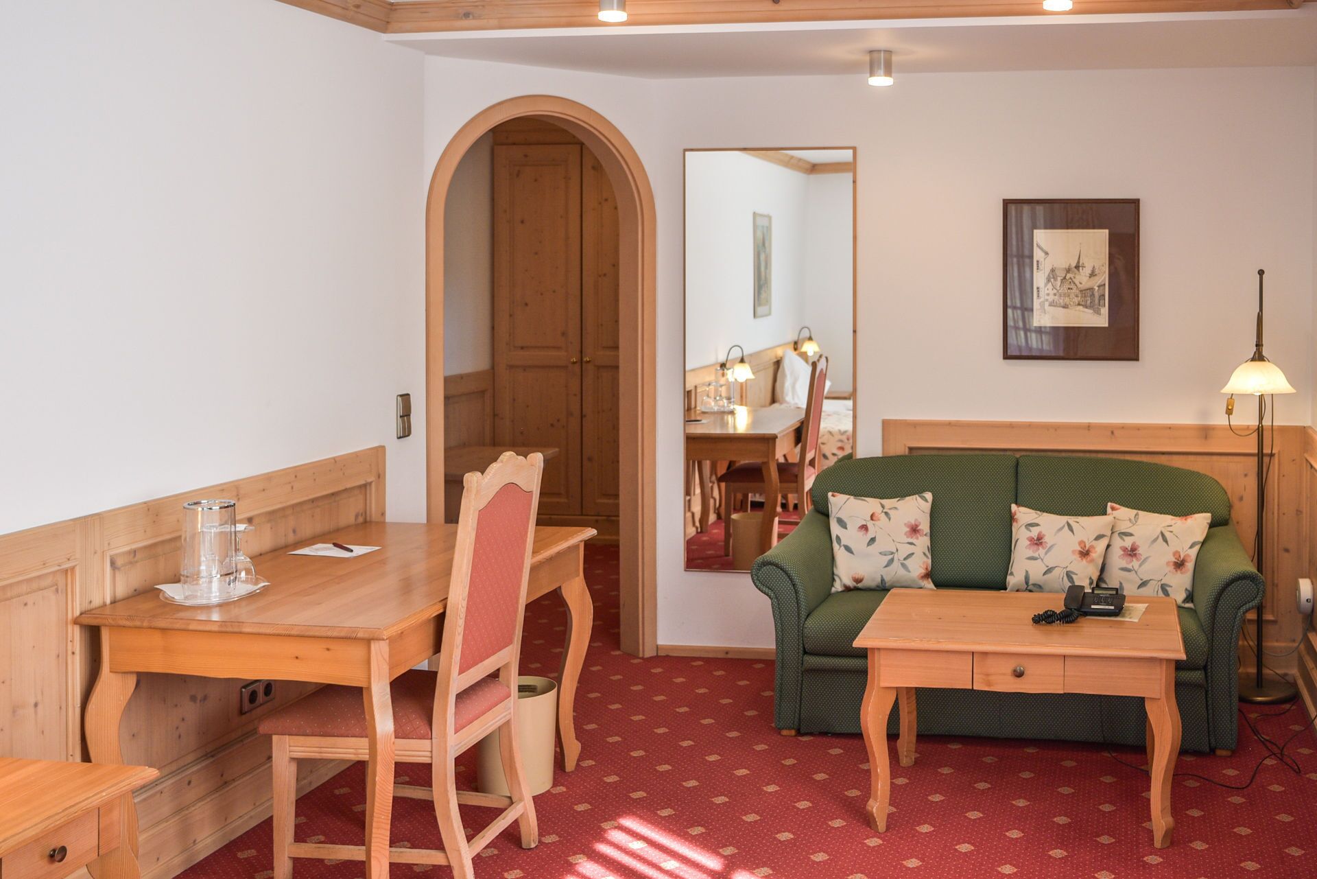 Una habitación acogedora con una mesa de comedor de madera, un sofá verde con cojines estampados y un escritorio de madera pequeño.