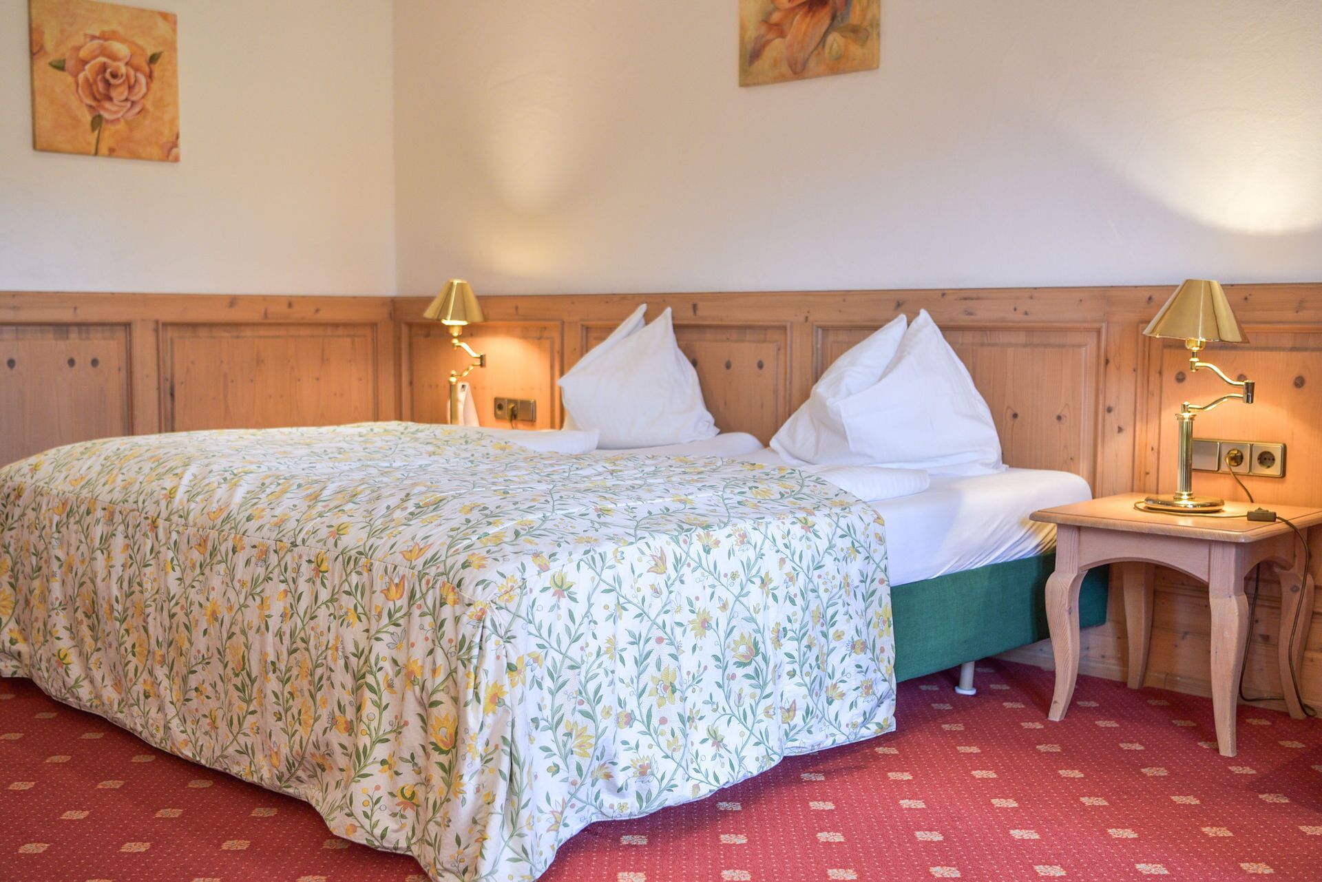 A neatly made bed with a floral bedspread, two bedside lamps, and a wooden headboard.