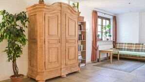A room with a large wooden wardrobe, a green potted plant, a plaid sofa, and a window with curtains. - Hotel Gasthof Süßer Grund (Albstadt)